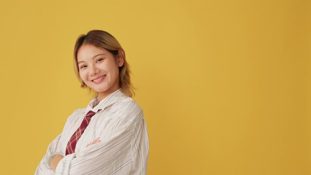 Young woman crosses her arms and looks at camera with smile isolated on yellow background