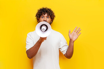young Indian man in a white T-shirt announces information into a loudspeaker on a yellow isolated...