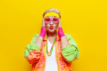 crazy funny old granny in sports colorful clothes and pink glasses on a yellow isolated background,...