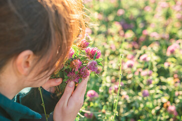 woman smells red clover. Womans face and red clover flowers in the rays of the sun in a clover field. Womens health flower