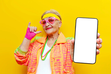 crazy funny old grandmother in sports colorful clothes shows a blank screen of a smartphone on a...