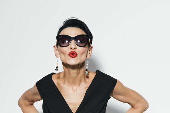 Sassy woman in stylish sunglasses and black dress striking a funny pose with hands on hips