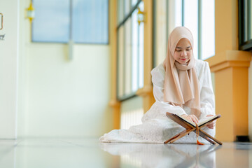 Ramadan, quran, The image of an Asian Muslim woman in the Islamic religion in hijab in cream color. reading the Quran and having a happy Staying in a beautiful mosque, Arabic word Holy Al Quran.