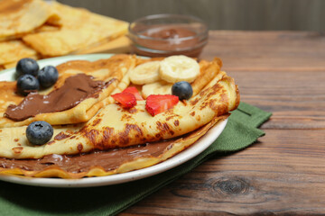 Tasty crepes with chocolate paste, banana and berries on wooden table, closeup