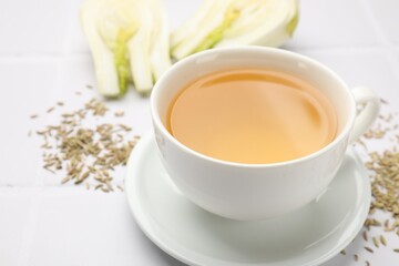 Fennel tea in cup, seeds and fresh vegetable on white tiled table, closeup
