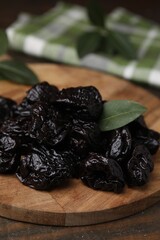 Tasty dried prunes and green leaf on wooden table, closeup