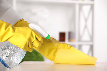 Woman with spray bottle and microfiber cloth cleaning white table at home, closeup. Space for text