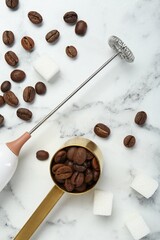 Milk frother wand, sugar cubes and coffee beans on white marble table, flat lay