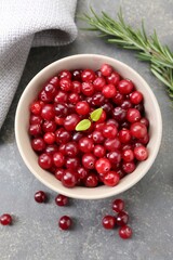 Fresh ripe cranberries in bowl and rosemary on grey table, flat lay