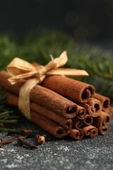 Different spices. Aromatic cinnamon sticks, clove seeds and fir branches on dark gray textured table, closeup