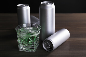 Energy drink with ice cubes in glass and aluminium cans on wooden table