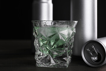Energy drink in glass and aluminium cans on wooden table, closeup
