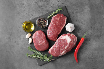 Raw beef steaks, oil and spices on grey background, top view