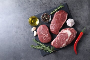 Raw beef steaks, oil and spices on grey background, top view. Space for text