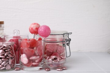 Tasty pink candies in glass jars on white background, closeup. Space for text