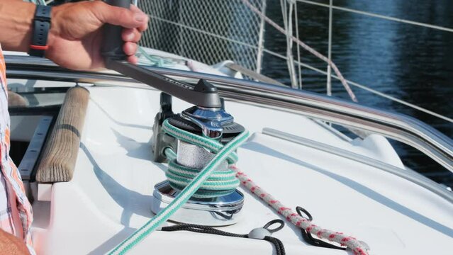 Seasoned yachtsman uses manual winch wrapping rope. Experienced skipper controls tension preparing lines before sailing in sea