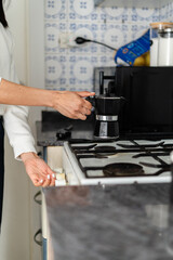 A person is using a moka pot on a gas stove, a traditional method of making rich espresso at home