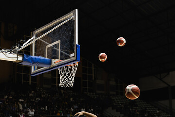 Couple of basketballs thrown into the ring in a basketball arena during a game in dark-almost-black...