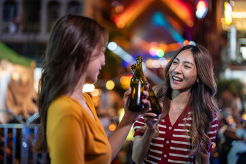 Asian woman friends hold bottle of beer, having party infront of bar. 