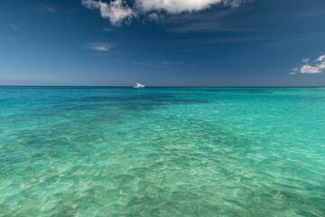 Fototapeta na wymiar Seascape with crystal clear shallow turquoise water, deep blue sky and white yacht on the horizon. Saona Island, Dominican Republic. Wide angle shot.