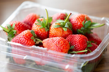 Strawberries in a plastic box on a wooden table, selective focus