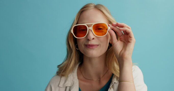 Woman, face and crazy with sunglasses in studio, happy and playful with protection from sun and eye care. Funky, goofy model in portrait and fashion frame with fun and retro style on blue background