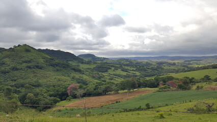 Fototapeta na wymiar Paisagem com montanhas verdes, área de terra preparada para plantação, e céu carregado de nuvens escuras