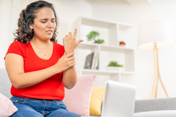 Woman Examining Wrist Pain While Working on Laptop