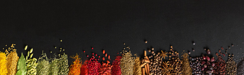 Colorful spices and herbs background. Seasoning for cooking food on black table with empty space.