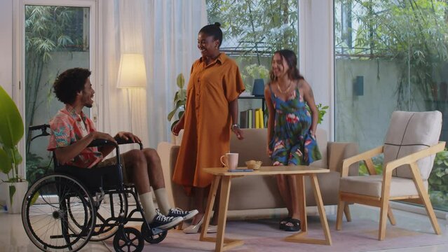 Wide shot of diverse young women meeting with friend with disability gathering at home