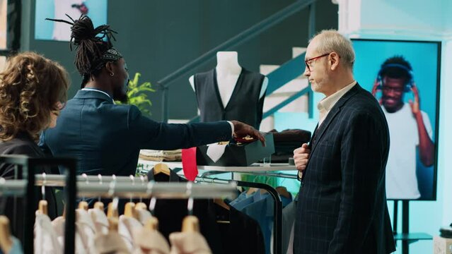 Fashion stylist making trendy recommendations for senior client, pairing an expensive tie to match a black elegant shirt. African american worker selling designer items to man. Camera A.