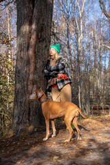 Pet owner with purebred dog magyar vizsla standing in pine forest, leaning to tree, warming in autumn sun, breathing fresh air, listening to silence, birds. Spending pastime with pleasure in nature