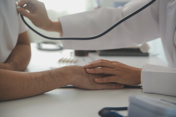 Fototapeta premium Young doctor is using a stethoscope listen to the heartbeat of the patient. Shot of a female doctor giving a male patient a check up