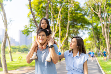 Happy Asian family enjoy and fun outdoor activity lifestyle on summer holiday vacation. Parents and little child daughter spending time exercising and playing together at public park in the city.