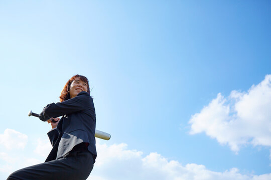 青空の下でバットを構えるスーツの女性