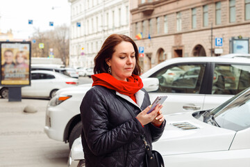 Fototapeta premium rental service concept. young Caucasian female woman calls taxi in smartphone app. woman looking for carshare car in smartphone app. transportation. female uses smart phone for checking latest news