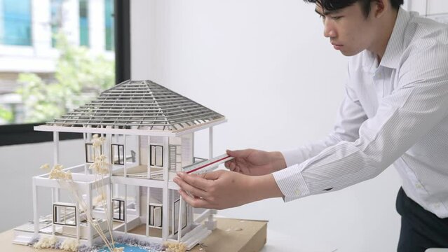 Close up of professional male architect engineer measure house model and using laptop analysis data at meeting table with house model and map . scatter around. Focus on hand. Immaculate.