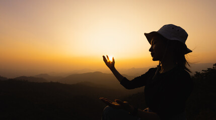 Silhuette Young Woman praying on the mountain, arms outstretched observing a beautiful dramatic...