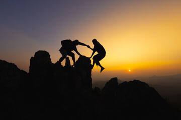  Silhouettes of two people climbing on mountain and helping. Teamwork of two men hiker helping each...