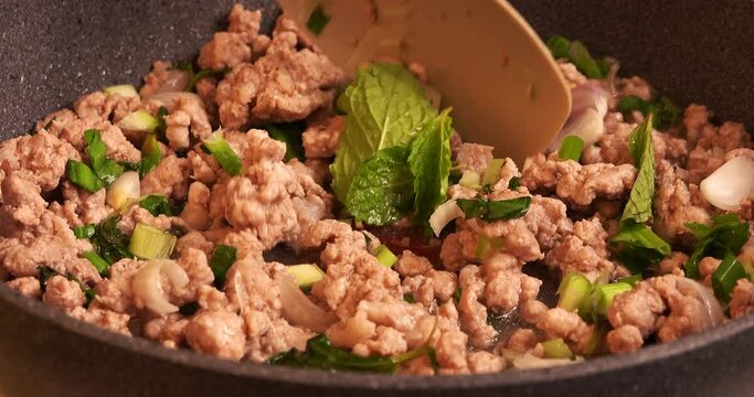 Close up view of adding Mint leaves into a pan to pan to mix with other ingredients for cooking Larb menu