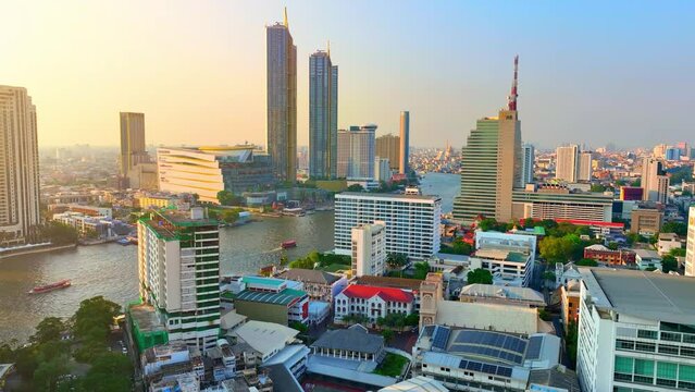 4K - Bangkok Thailand: Aerial view, Urban skyline painted in sunset hues, skyscrapers flank the river as a drone hovers over downtown's bustling business district. World destination concept.

