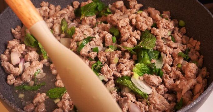  Close up view of video footage of mixing and stirring ingredients for cooking Larb with minced pork in a pan, tilting from right to left