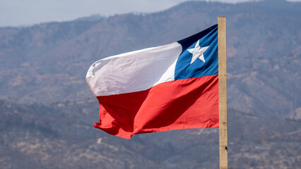 Naklejka premium bandera chilena en mastil de madera sin pintar, de fondo se ve un cerro o montaña desenfocado