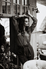 Young Caucasian woman in an orange blouse and green trousers. Against the background of an authentic old wooden wall. Green plants in the background. Concept: fashion retail or lifestyle blog.