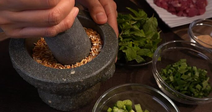 Slow Motion of grinding roasted rice in a stone mortar in Thai style, preparing ingredients for cooking Larb menu