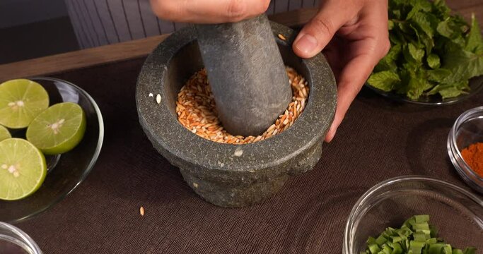 Video Footage of Grinding roasted rice in a stone mortar in Thai style, preparing ingredients for cooking Larb menu