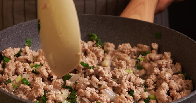 Video footage of mixing and stirring ingredients for cooking Larb with minced pork in a pan, tilting camera from top to bottom