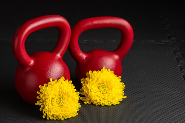 Chinese (Lunar) New Year fitness, red kettlebell on a black gym floor with a bright yellow Chinese chrysanthemum flower

