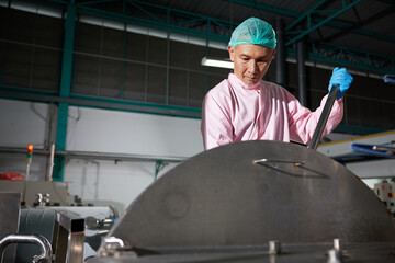 worker stirring water on large industrial pot in the factory