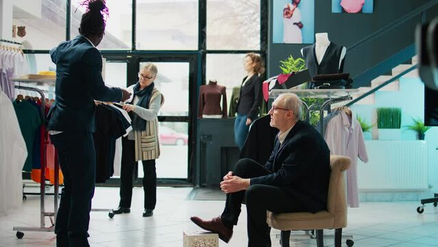 Senior man trying on elegant leather shoes for a special occasion, shopping for classy high quality footwear at clothing store. African american retail assistant helping customer. Camera B.
